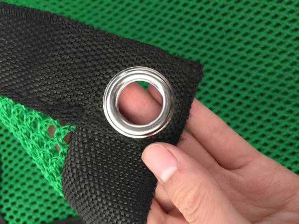 A hand is holding the button hole of  green flexible windbreak netting.